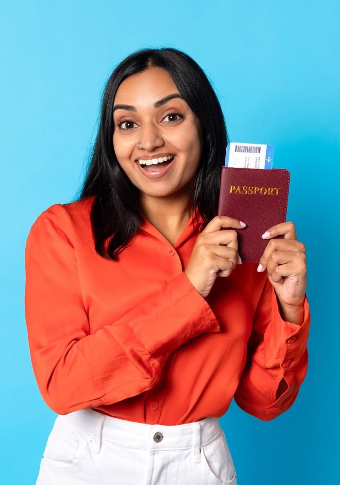 Happy young indian lady traveler showing passport and boarding pass in blue studio, smiling to camera and promoting travel offer for millennials, modern holiday advertisement banner