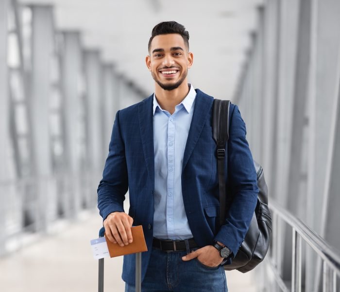 Portrait Of Young Middle Eastern Male Traveller Posing At Airport, Handsome Arab Man With Luggage, Passport And Tickets Smiling At Camera While Waiting For Flight In Terminal, Copy Space